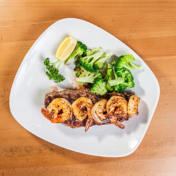Grilled steak and shrimp with broccoli, parsley, and a lemon wedge on a white plate.