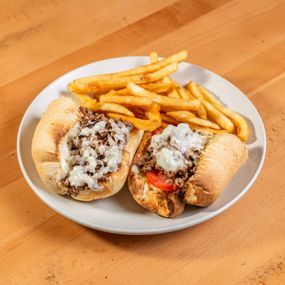 Two Rincon Italiano cheesesteak sandwiches with melted cheese, meat, and tomatoes, served with fries.