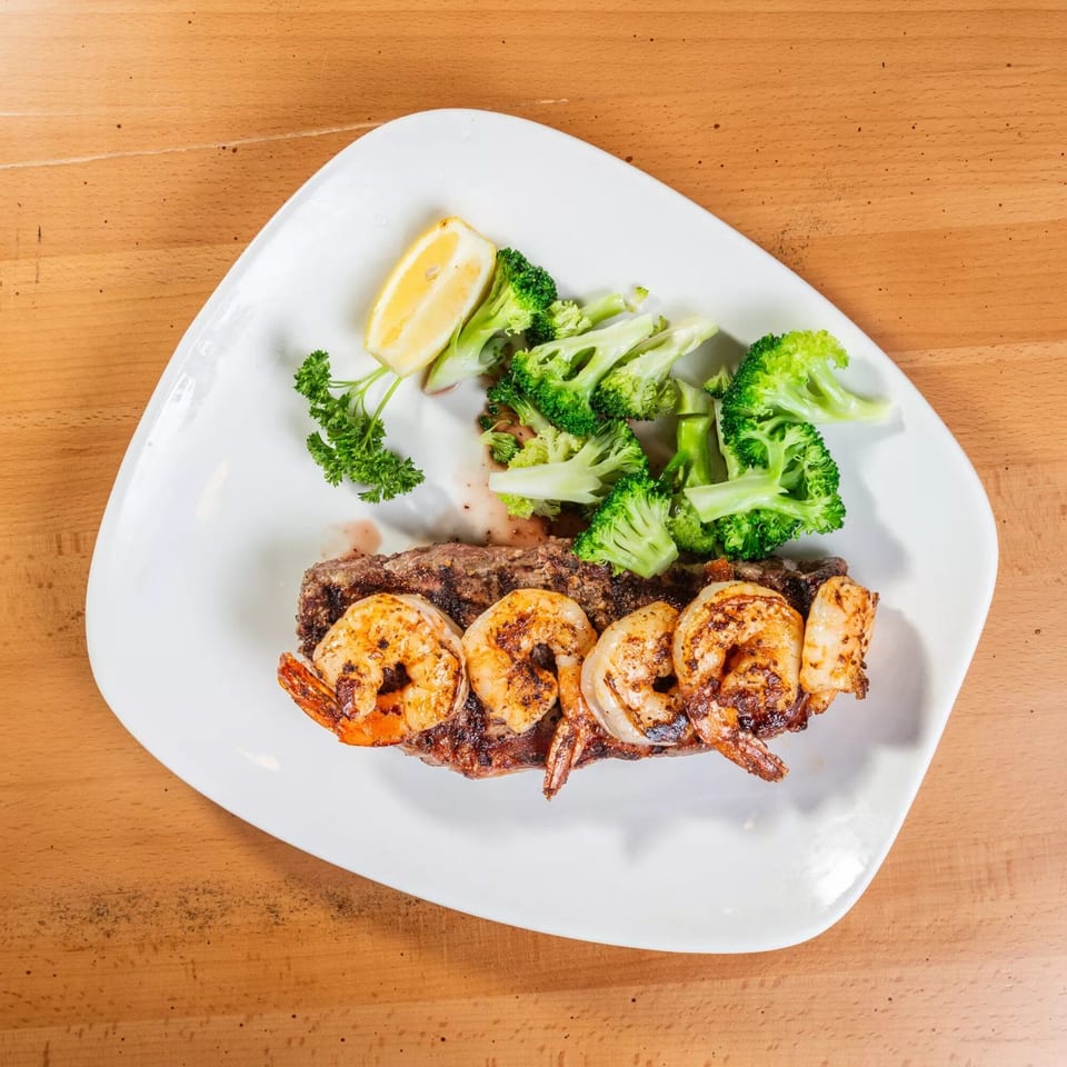Grilled steak and shrimp with broccoli, parsley, and a lemon wedge on a white plate.