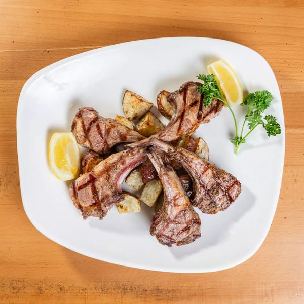 Grilled lamb chops with roasted potatoes, lemon wedges, and parsley on a white plate.