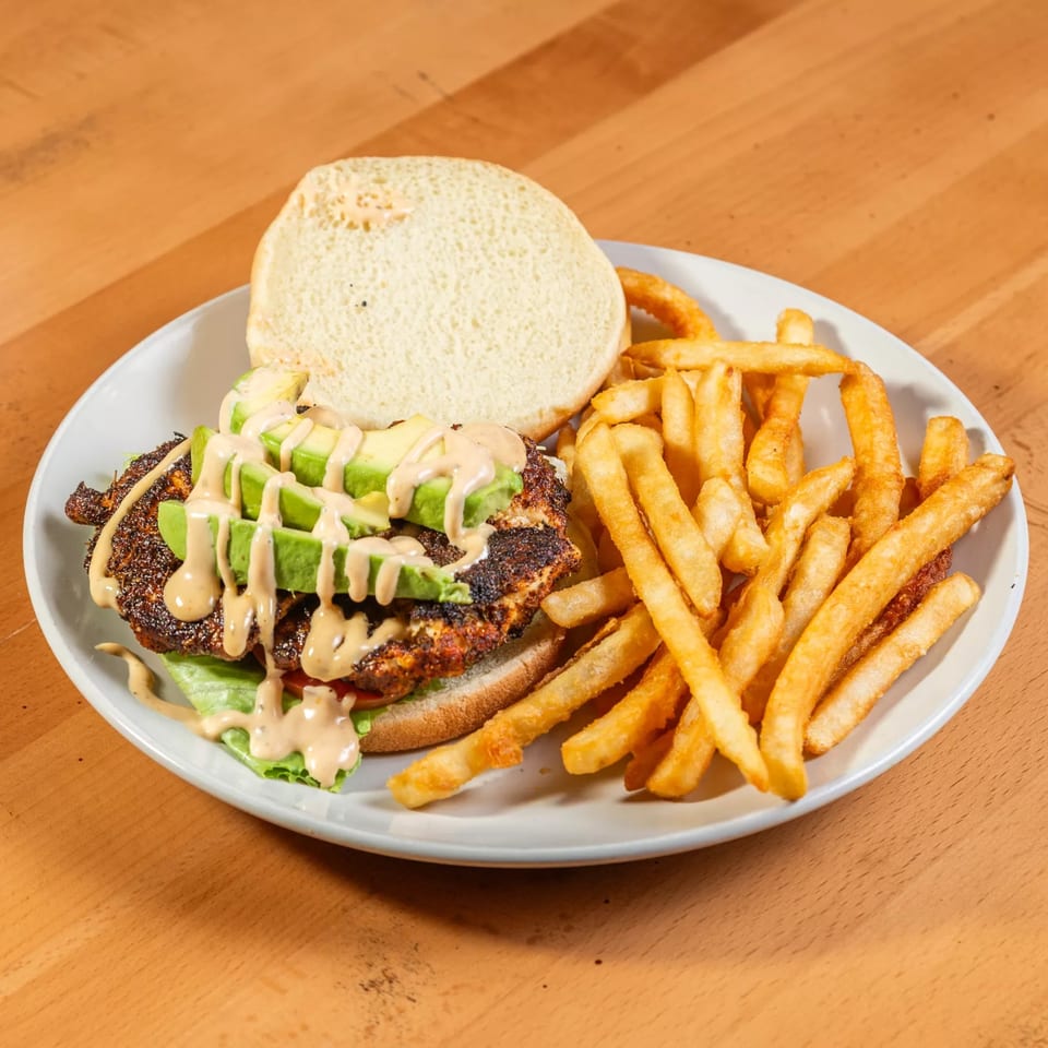 Open-faced chicken sandwich with avocado and sauce, served with a side of french fries.